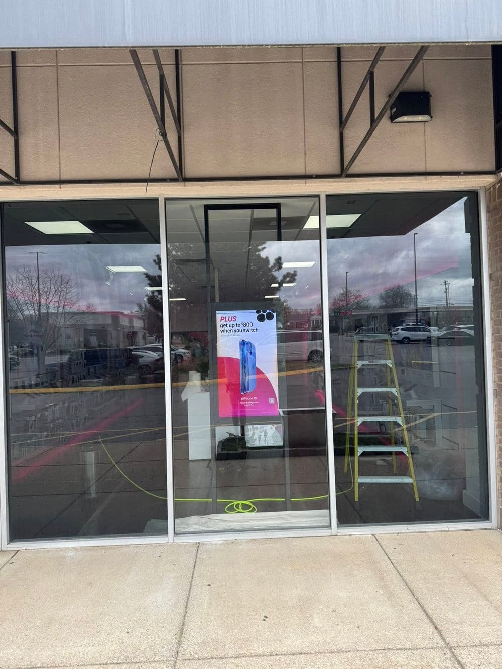 Storefront display with promotional poster for smartphone, ladder visible outside.
