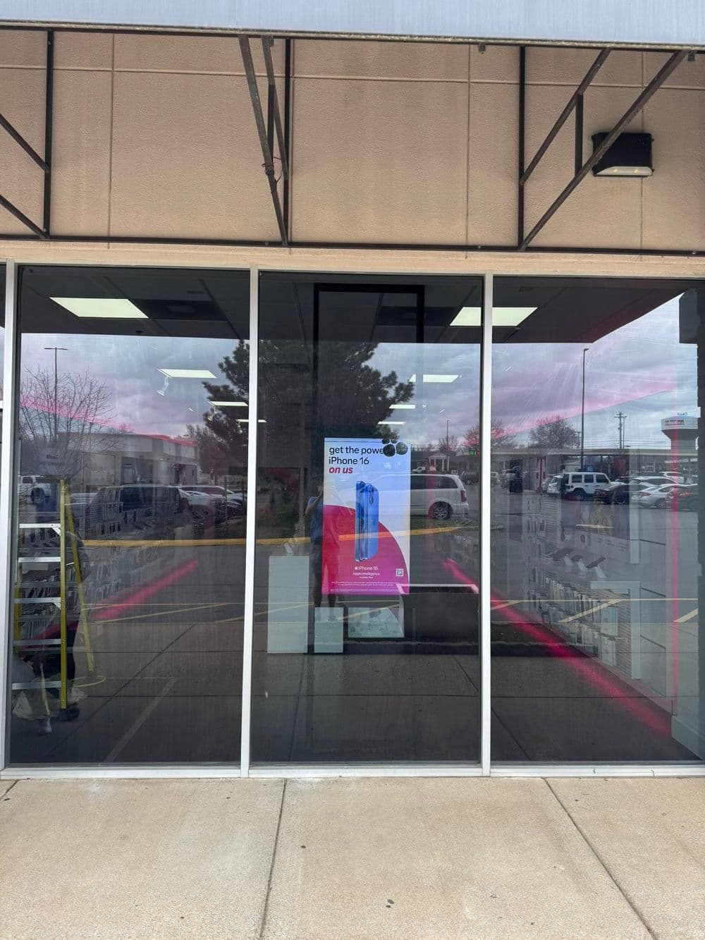 Storefront with promotional poster for power tools, reflecting outdoor scene and bright sky.