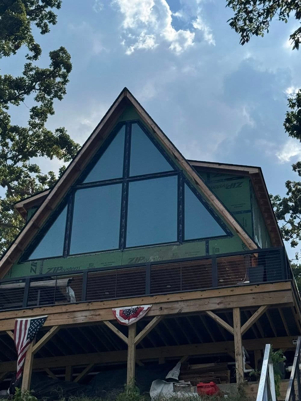 A-frame cabin under construction with large windows and American flags, set in wooded area.