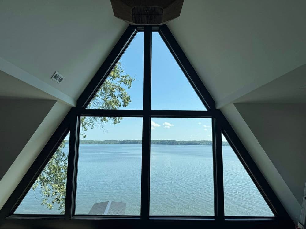 A-frame cabin window with panoramic lake view and clear blue sky.