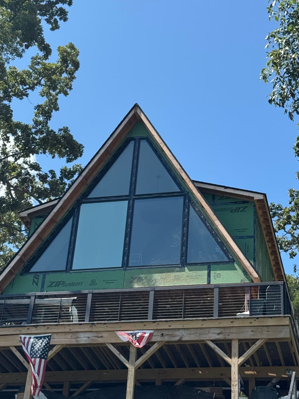 A-frame cabin with large windows and green construction materials under a blue sky.