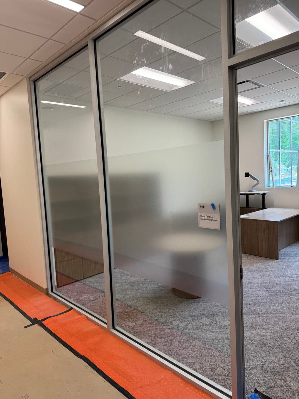 Frosted glass office partition with an empty workspace and modern decor visible inside.