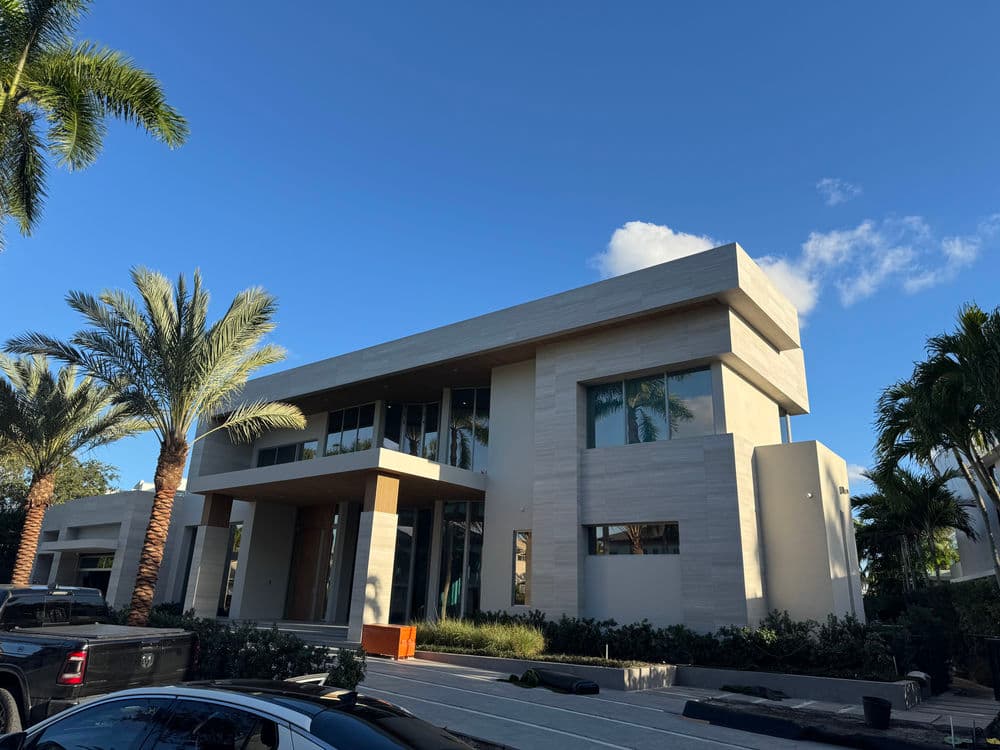 Modern luxury home with large windows, palm trees, and blue sky. Stylish design and landscaping.
