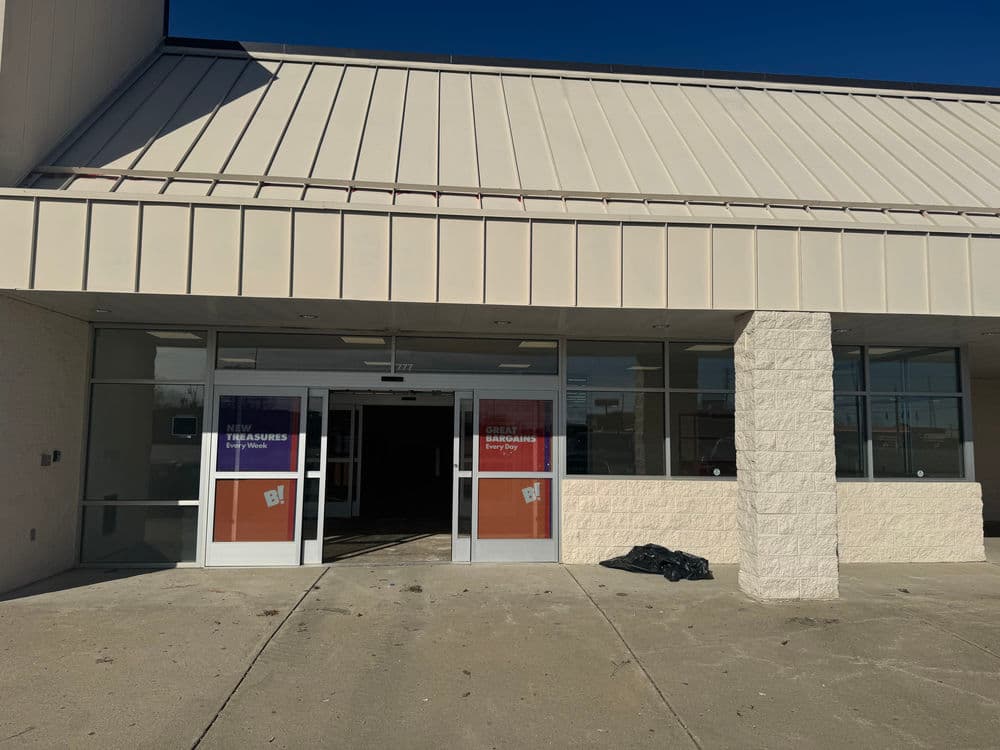 Abandoned storefront entrance with large glass doors and signage in a commercial building.